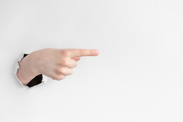 Child hand pointing the forefinger to the right through hole in white paper with torn edges concept of attention with copy space