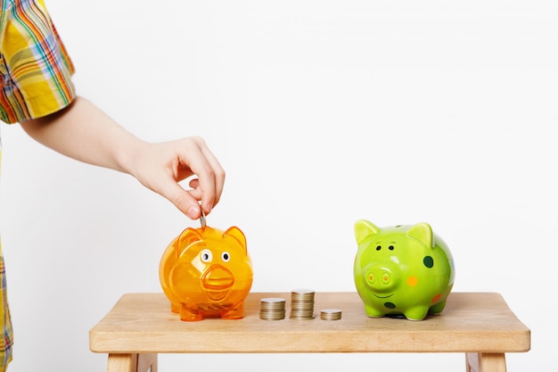 Child hand putting coin in a piggy bank.