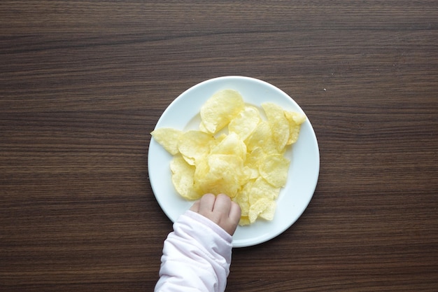 Child hand reaching for potato chips on a plate