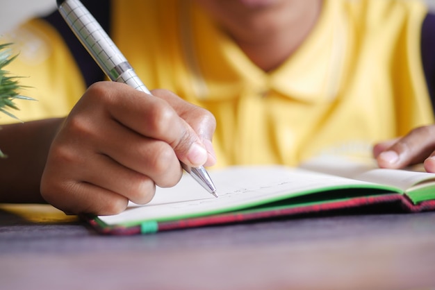 Scrittura della mano del bambino sul shile del blocco note seduto