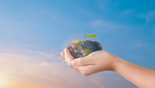 Photo child hands holding apple globe earth over blurred sunset sky background world environment day concept