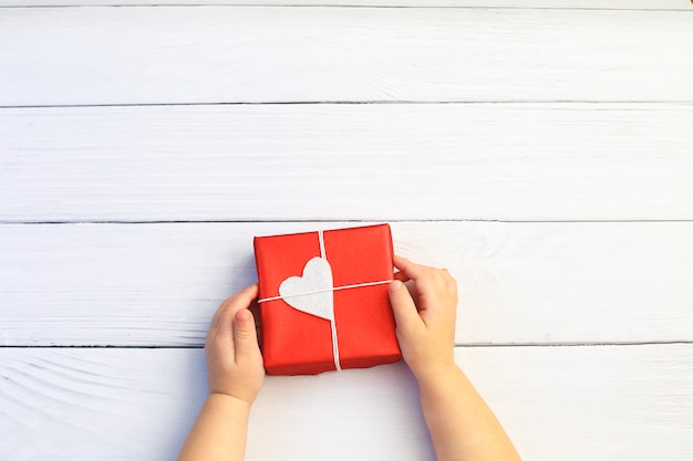 Foto le mani del bambino che tengono il bello contenitore di regalo su fondo di legno