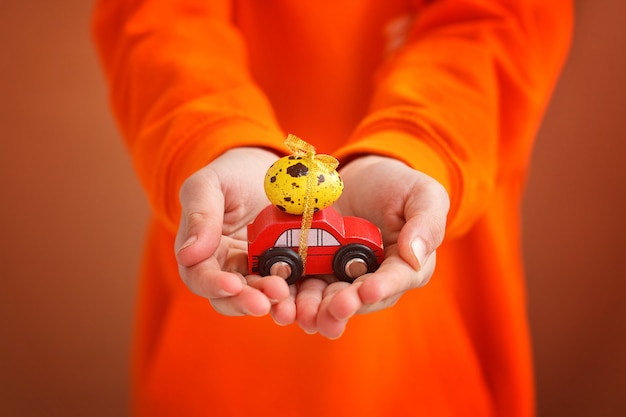 Руки ребенка, держа пасхальное яйцо на машине на оранжевом фоне. Счастливой Пасхи концепции.