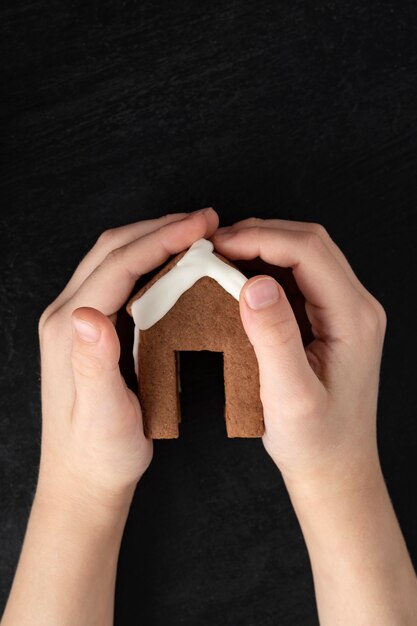 Child hands holding gingerbread house. Top view, black background.