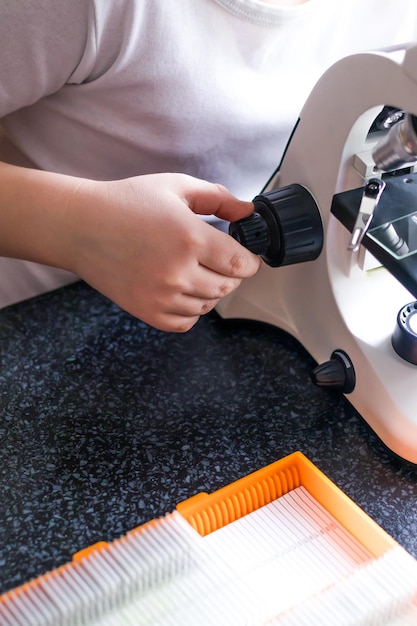 Детские руки устанавливают стекло с лабораторными материалами в микроскоп для исследований. Научное образование