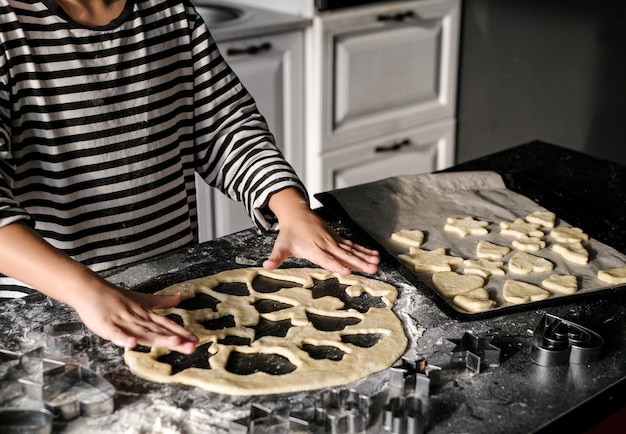 Child hands is making a christmas cake at kitchen with forms