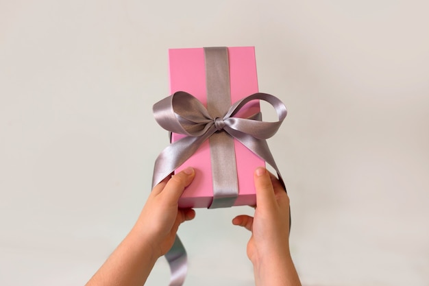 Photo child hands picking up a pink gift with silver ribbon