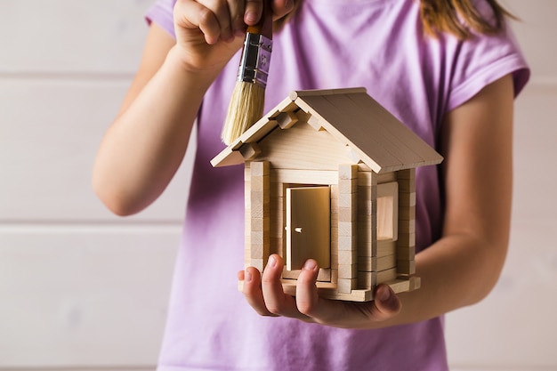 Фото Детские руки с игрушечным деревянным домом и малярной кистью