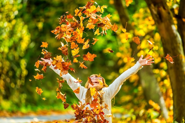 Child happily throwing orange leaves above her during autumn.