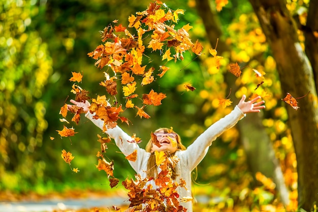 Bambino che lancia felicemente foglie d'arancio sopra di lei durante l'autunno.