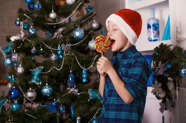 child happy eating candy near christmas tree