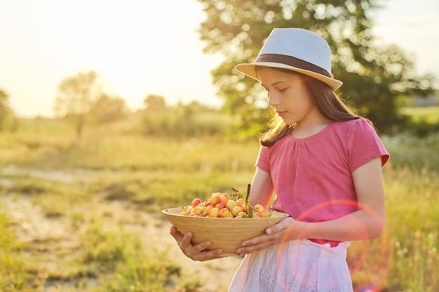 Child in hat with bowl of yellow sweet cherry