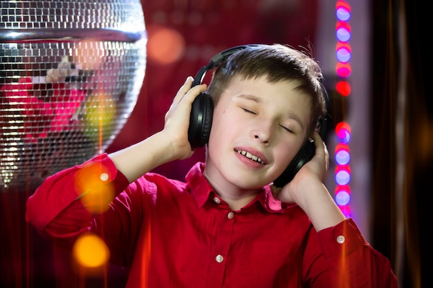 A child in headphones listens to music against the background of a disco ball.