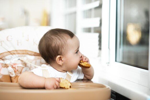 A child in a high chair eating a cracker with raisins