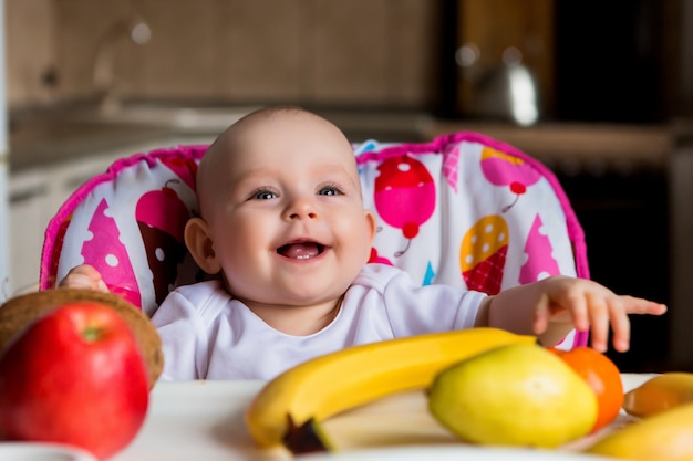 ребенок в высоком стуле ест фрукты и улыбается
