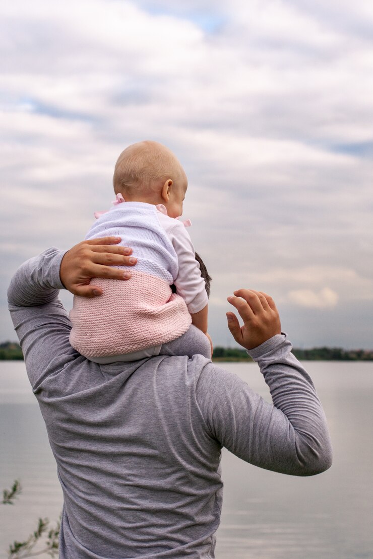 Photo a child on his father neck. walk near the water. baby and dad against the sky.