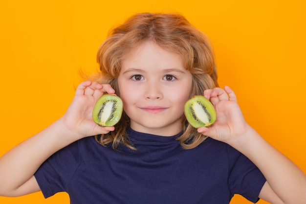 Child hold kiwi in studio Kiwi fruit Studio portrait of cute kid boy with kiwi isolated on yellow