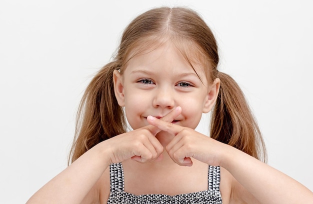 Photo child holding crossed fingers on mouth