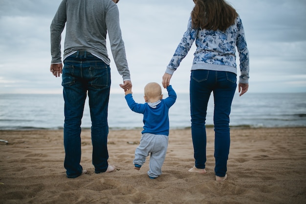 Child holding hands of his parents and walking on the sand.