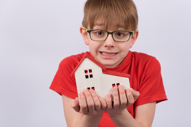 Child holding model of house on white wall