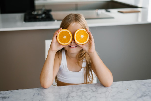 child holding orange slice in front of her eyes at the kitchen table