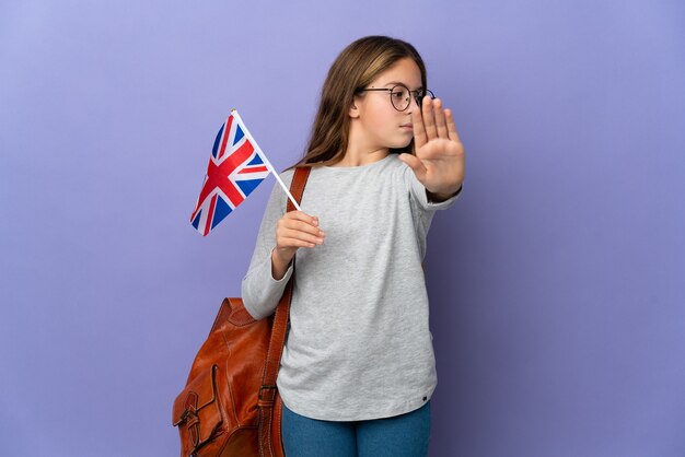 Ребенок держит флаг Соединенного Королевства на изолированном фоне, делая жест стоп и разочарованный