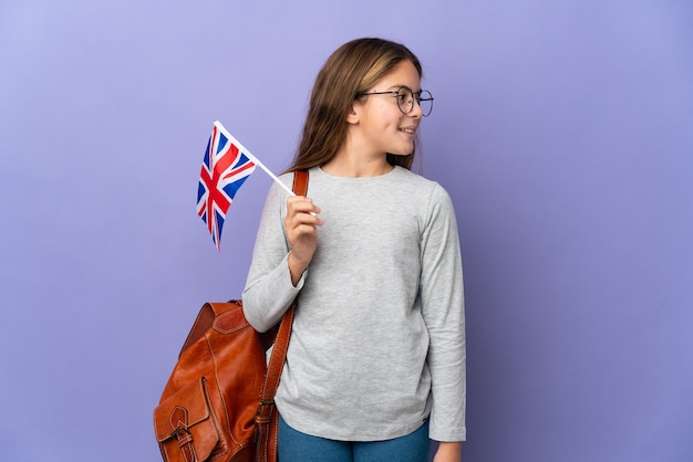 Child holding an United Kingdom flag over isolated wall looking side