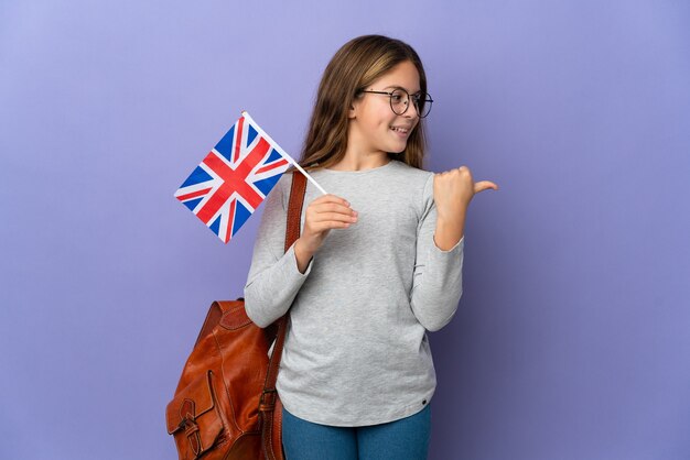 Child holding an United Kingdom flag over isolated wall pointing to the side to present a product