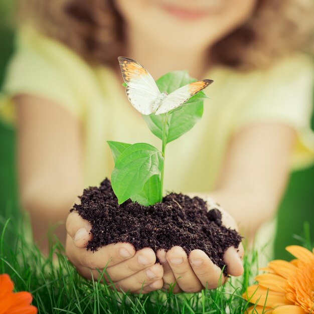 春の緑の背景のエコロジーとアースデイの概念に対して若い植物を手に持っている子供