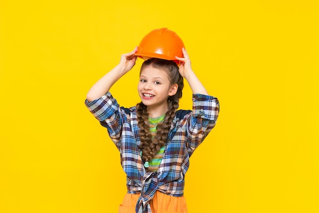 A child holds a construction helmet over his head A little girl is getting ready for renovation in the children's room The profession of an engineer Yellow isolated background