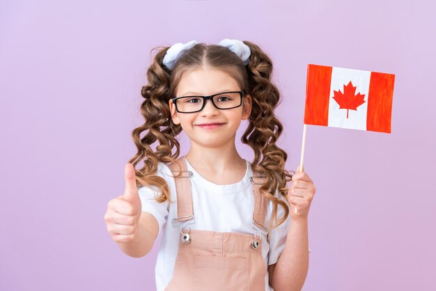 The child holds the flag of Canada and smiles Canadian school education child on an isolated purple background