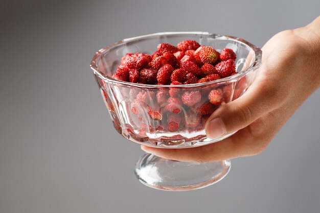 A child holds a glass bowl with ripe red strawberries. Close up.