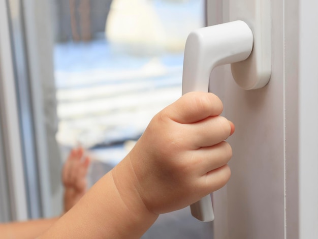 The child holds on to the handle of the window trying to open it. The concept of leaving only children at home, the safety of children, children without parental supervision