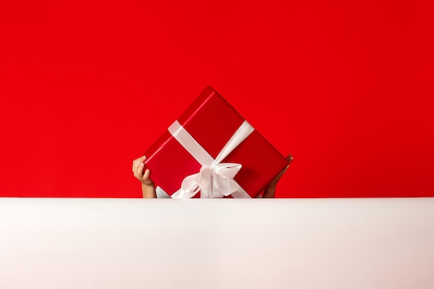 Child holds in his hands a large box with a satin white bow\
hiding behind it