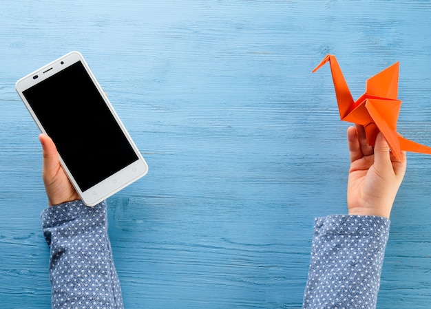 Foto il bambino tiene tra le mani un telefono e una gru origami