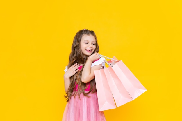 A child holds paper bags with purchases after shopping sale and shopping for little girls a charming girl holds gift bags on a yellow isolated background