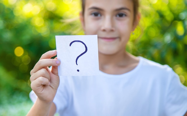 The child holds a paper with a question mark. Selective focus. Kid.