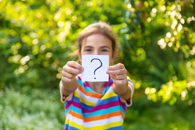 The child holds a paper with a question mark. Selective focus. Kid.