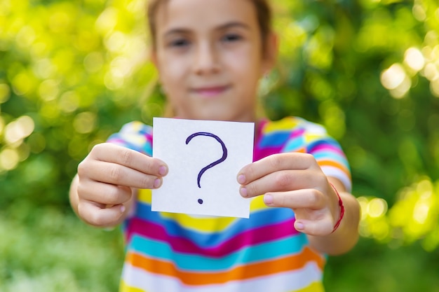 The child holds a paper with a question mark. Selective focus. Kid.