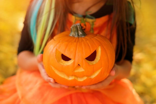 A child holds a pumpkin with a carved sinister smile in his hands