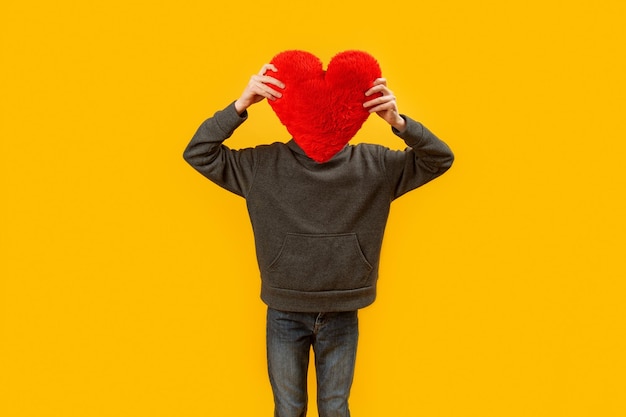 Ребенок держит красную подушку в форме сердца Мужчина с плюшевым сердцем вместо головы Скопируйте пространство Желтый фон