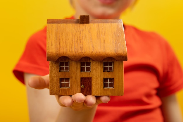 Il bambino tiene una piccola casa di legno sul palmo della mano concetto di casa e comfort alloggio e mutuo propri primo piano