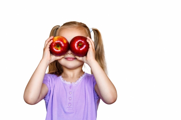 The child holds two red apples in front of her eyes