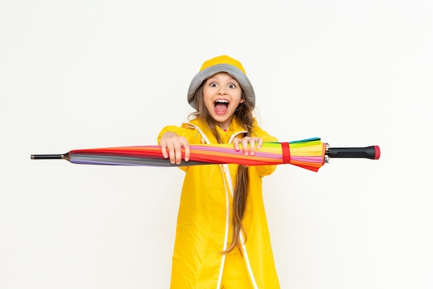 The child holds the umbrella horizontally and smiles broadly A little girl in a yellow raincoat and a panama hat on a white isolated background