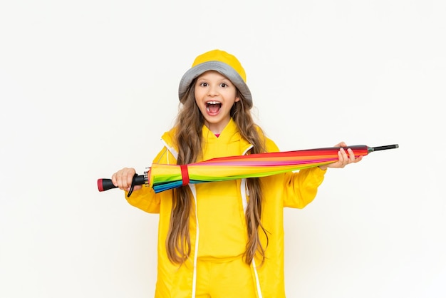 The child holds the umbrella horizontally and smiles broadly A little girl in a yellow raincoat and a panama hat on a white isolated background