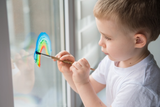 Child at home draws a rainbow on the window