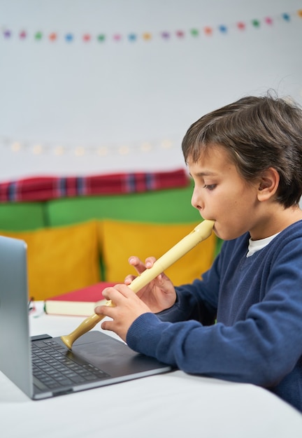 Child at home learning to play the flute with an online teacher connected with the laptop