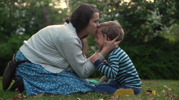 Child is crying in park in arms of mom mommy soothes baby boy\
family mother and child with tears