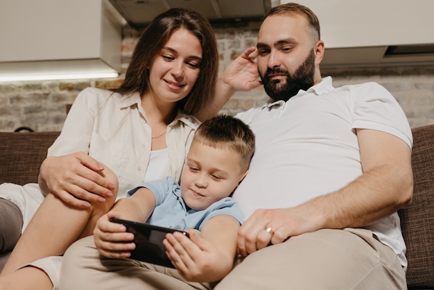 A child is demonstrating a cartoon on the smartphone to mother and father in the evening at cozy home