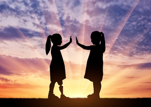 The child is a disabled girl with a prosthetic leg and her friend in the open air at sunset. The concept of childhood of disabled children with leg prosthesis